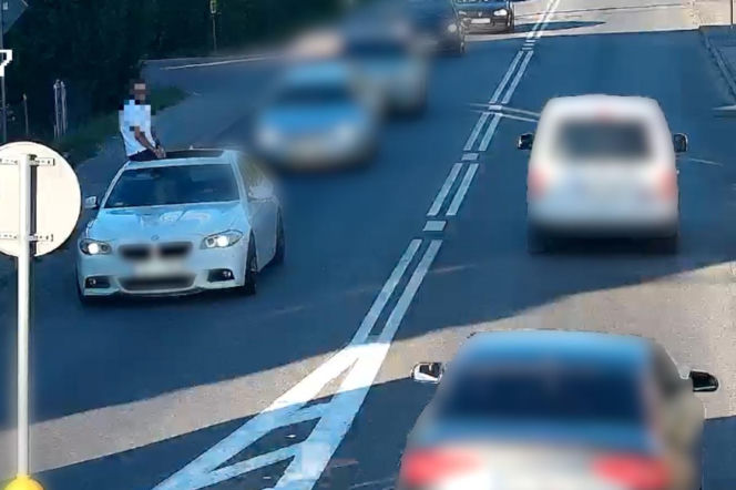Mężczyzna siedzący na dachu jadącego białego BMW na ulicy w Jaśle. O incydencie przeczytasz na Eska Rzeszów.