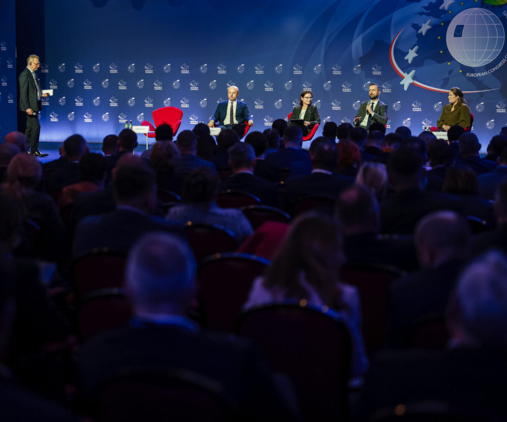 Prelegenci i goście podczas panelu dyskusyjnego na XI Europejskim Kongresie Samorządów w Mikołajkach. W tle scena z logo wydarzenia i grafikami województwa warmińsko-mazurskiego. Więcej informacji o Kongresie na Super Biznes.