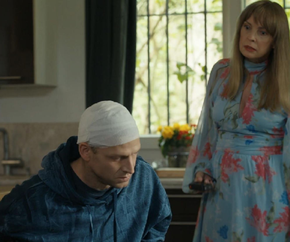 Agnieszka (Katarzyna Tlałka) w kwiecistej sukience i Łukasz (Michał Rolnicki) z zabandażowaną głową, przykuty kajdankami do stołu, w scenie z serialu Barwy szczęścia. Zdjęcie ilustruje dramatyczne wydarzenia z 3299. odcinka, o których możesz przeczytać na portalu Super Seriale.