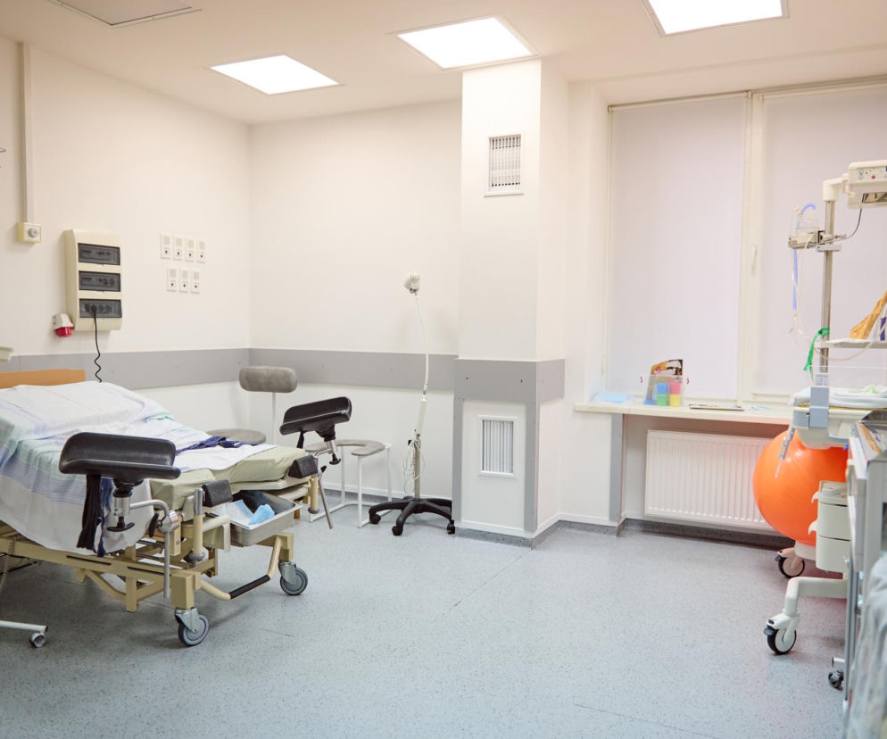 Czysta sala porodowa w szpitalu, z łóżkiem porodowym, kroplówką, piłką do ćwiczeń i sprzętem medycznym, symbolizująca miejsca, o których czytasz na Poradnik Zdrowie w kontekście śmierci pacjentki po porodzie.