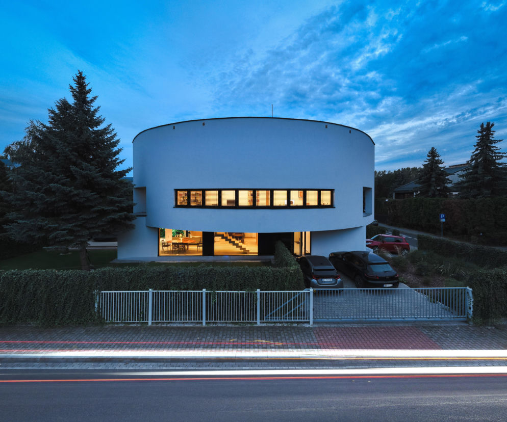 Biały dom o kształcie półksiężyca wieczorem. O przebudowie budynku w Warszawie przeczytasz w serwisie Architektura.