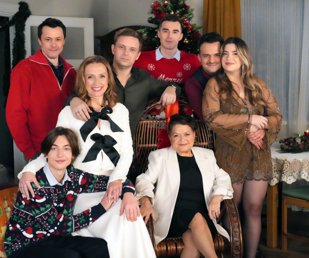 Rodzinne zdjęcie aktorów z serialu Barwy szczęścia uśmiechających się w świątecznych strojach przed choinką. Lucyna (Bożena Stachura), Asia (Anna Gzyra), Hubert (Marek Molak), Daniel (Marcin Bikowski), Staś (Olaf Kaprzyk) i inni bohaterowie świętują, co zapowiada dziwne święta u Pyrków, o których przeczytasz na Super Seriale.