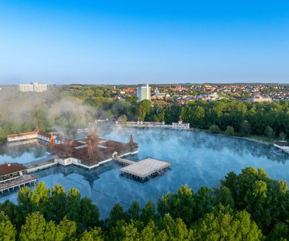 Widok z góry na parujące jezioro termalne Hévíz z drewnianymi pawilonami kąpieliska. O wellness na Węgrzech czytaj w Eska.