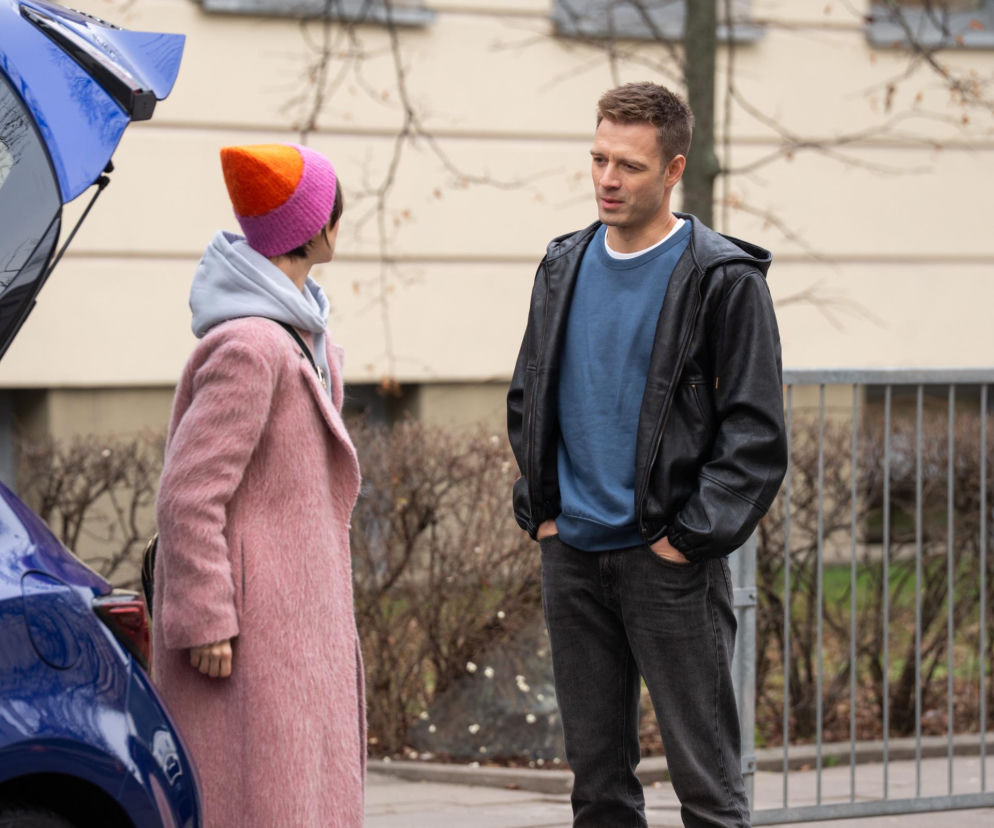 Kadr z serialu Na dobre i na złe. Mario (Marcin Korcz) w czarnej skórzanej kurtce i niebieskiej bluzie, stoi obok otwartego bagażnika niebieskiego samochodu. Rozmawia z Blanką (Pola Gonciarz), która ma na sobie różowy płaszcz i kolorową czapkę. Więcej o tym, co dalej w ich relacji, dowiesz się na Super Seriale.