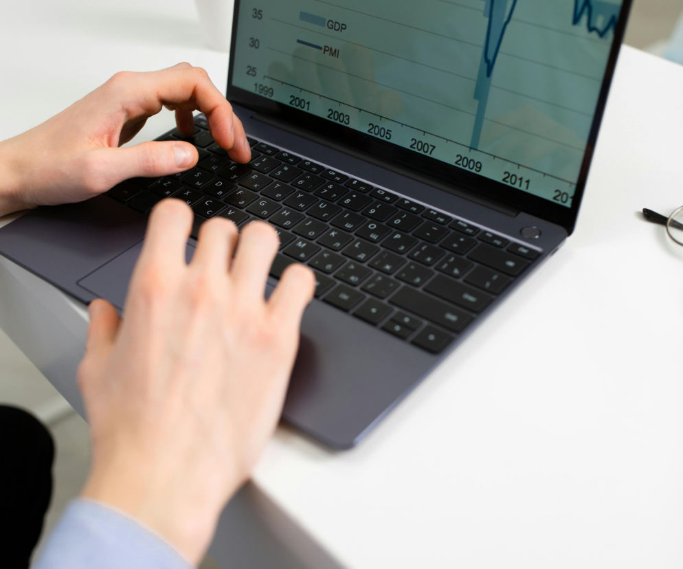 Osoba wpisująca dane na laptopie z wykresem wzrostu gospodarczego, symbolizującym prognozy ekonomiczne Polski na 2026 rok, w tym wzrost inwestycji i PKB. O perspektywach gospodarczych w Polsce przeczytasz na Super Biznes.