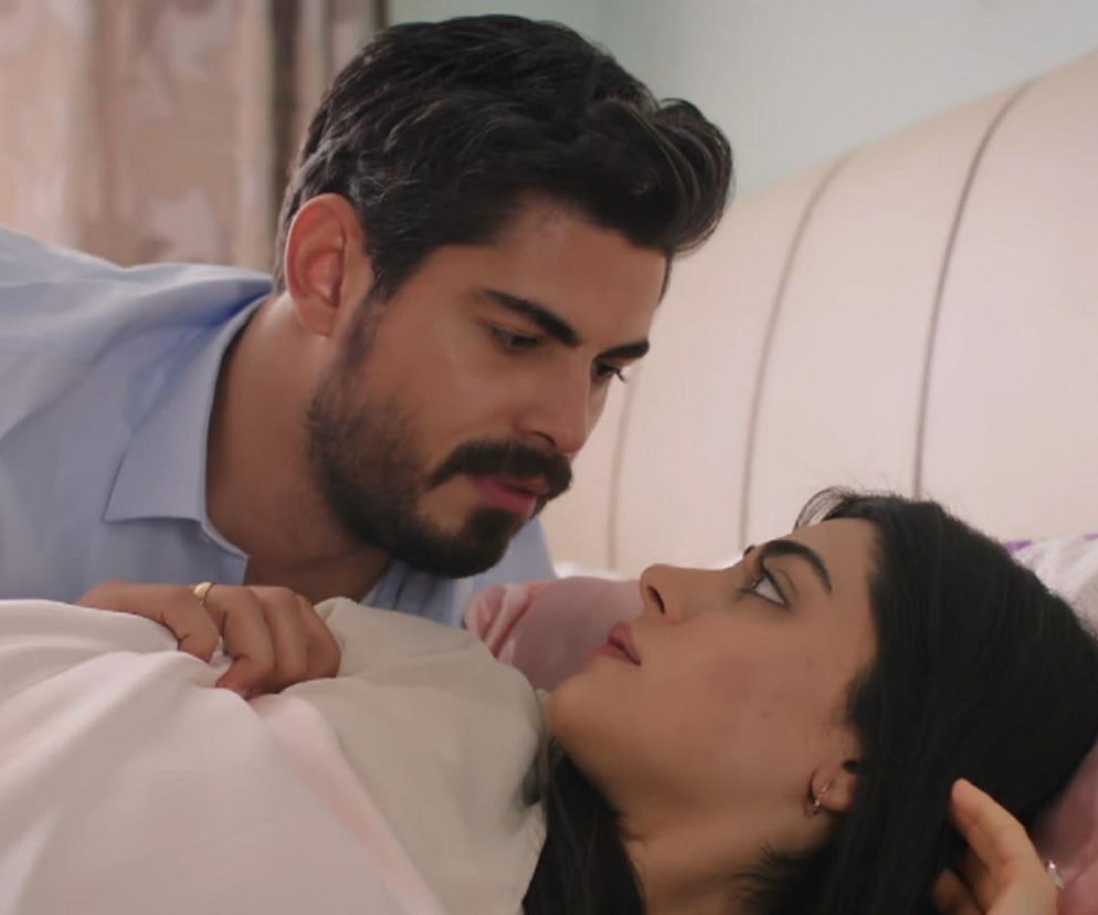 Intensywne spojrzenie Cihana na Hancer w łóżku, gdy oboje leżą pod białą pościelą. On ma jasnoniebieską koszulę, ona ciemne włosy rozłożone na poduszce. Zdjęcie przedstawia scenę z odcinków tureckiego serialu Panna Młoda dostępnego na Super Seriale.