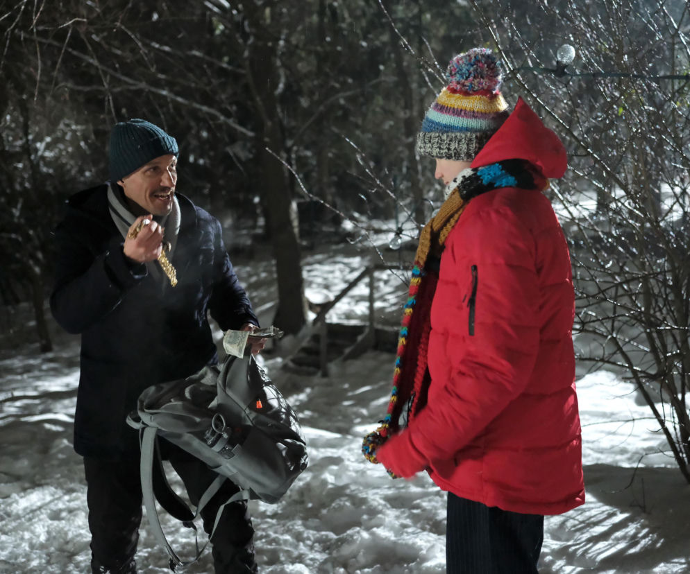 Franek (Jarosław Śmigielski) w zimowej czapce i czerwonej kurtce oddaje ojczymowi (Marcin Sitek) skradzione złote naszyjniki i pieniądze w ośnieżonym lesie. Ojczym trzyma gotówkę i plecak. Więcej o dramatycznych wydarzeniach w M jak miłość przeczytasz na Super Seriale.