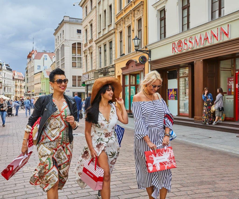 Trzy uśmiechnięte kobiety z torbami idą obok drogerii Rossmann. O promocji na maseczkę Kimoco przeczytasz na SE.