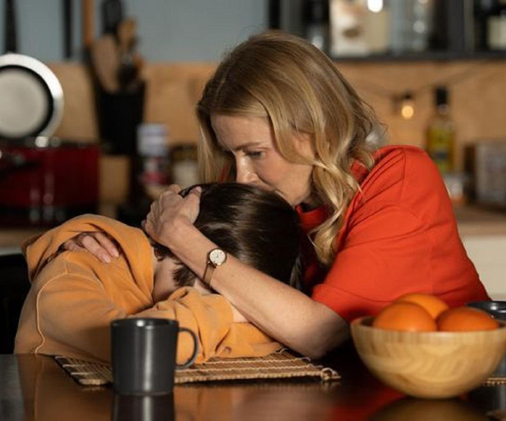 Dominika (Karolina Chapko) pocieszająca zrozpaczonego Mateuszka (Filip Kowalewicz) w serialu Barwy szczęścia. Chłopiec ma głowę opartą na rękach, a kobieta trzyma dłoń na jego głowie i całuje go w czoło, chcąc dodać mu otuchy. Więcej na Super Seriale.