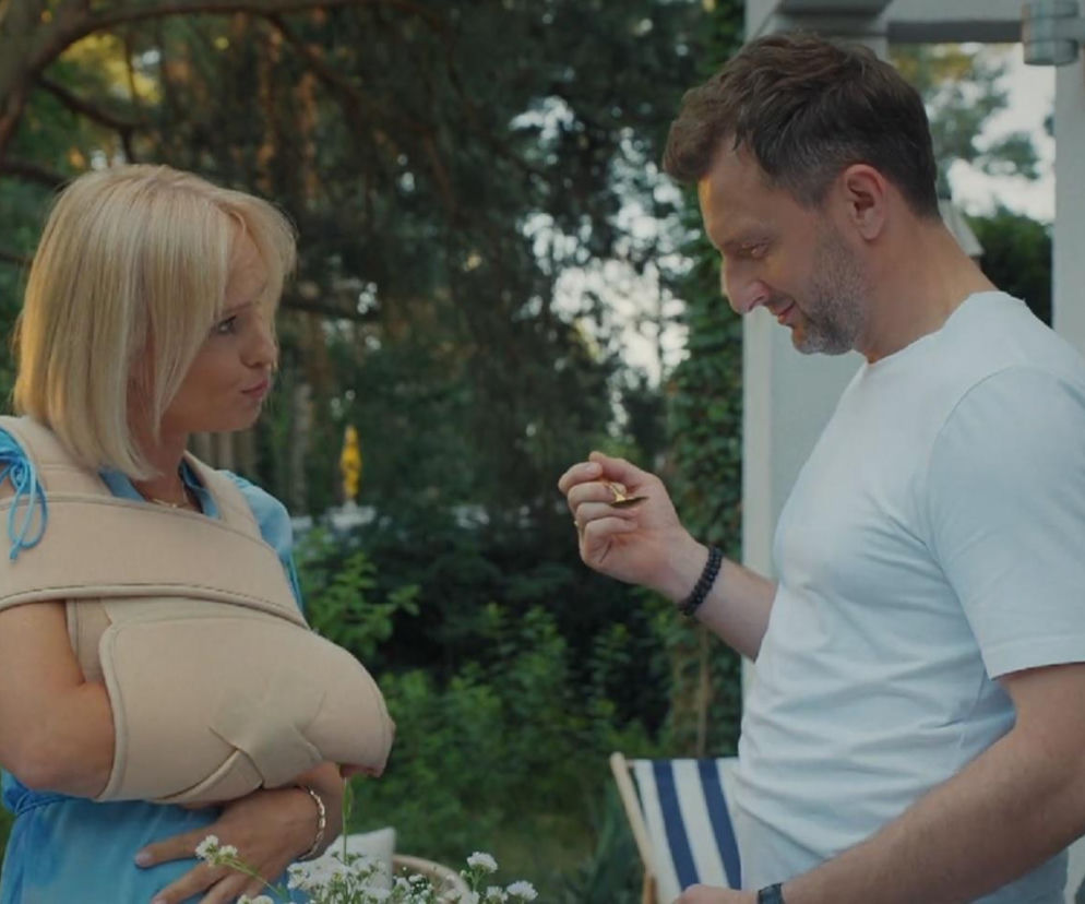 Iwona Rejzner jako Dorota w niebieskiej sukience, z jasnymi włosami i ręką w beżowym temblaku, patrzy na Arkadiusza Smoleńskiego jako Bartka, który w białej koszulce trzyma w dłoni mały, złoty przedmiot, najprawdopodobniej klucz. Tę scenę i inne Super Seriale można zobaczyć na portalu.