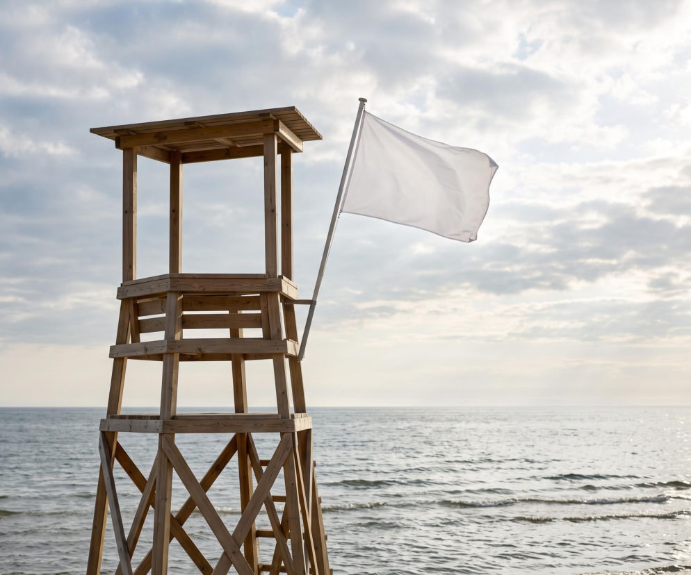 Drewniana wieża ratownika z białą flagą na plaży w Darłowie. O bezpiecznych kąpielach przeczytasz na SE Szczecin.