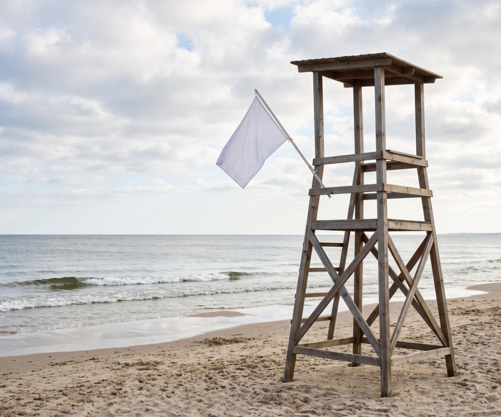 Drewniana wieża ratownika z białą flagą na plaży. O bezpiecznych kąpieliskach w Gdańsku przeczytasz na Eska Trójmiasto.