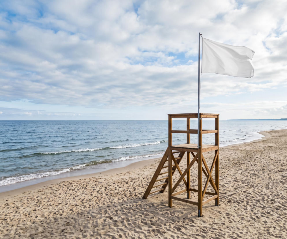 Drewniana wieża ratownicza z białą flagą na plaży w Trzęsaczu. O bezpiecznej kąpieli przeczytasz na SE Szczecin.