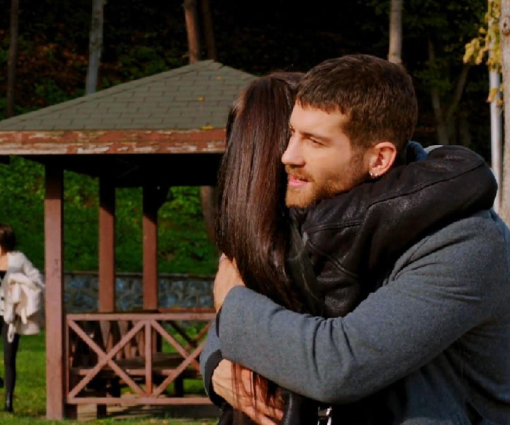 Cihan w czarnej kurtce i szarym płaszczu obejmuje kobietę w parku, a w tle widać altanę. Z boku widać Zeynep i Egego, którzy śledzą Cihana w 338. odcinku serialu „Miłość i nadzieja”. Więcej informacji znajdziesz na Super Seriale.