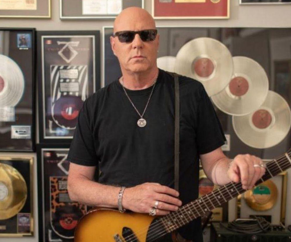 Gitarzysta Twisted Sister Jay Jay French trzyma gitarę na tle złotych płyt. O sporze z Hall of Fame przeczytasz w EskaRock.