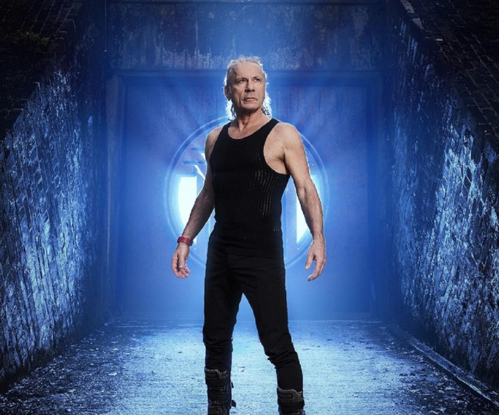 Bruce Dickinson w czarnym stroju na tle tunelu z niebieskim światłem. O liderze Iron Maiden czytaj na EskaRock.