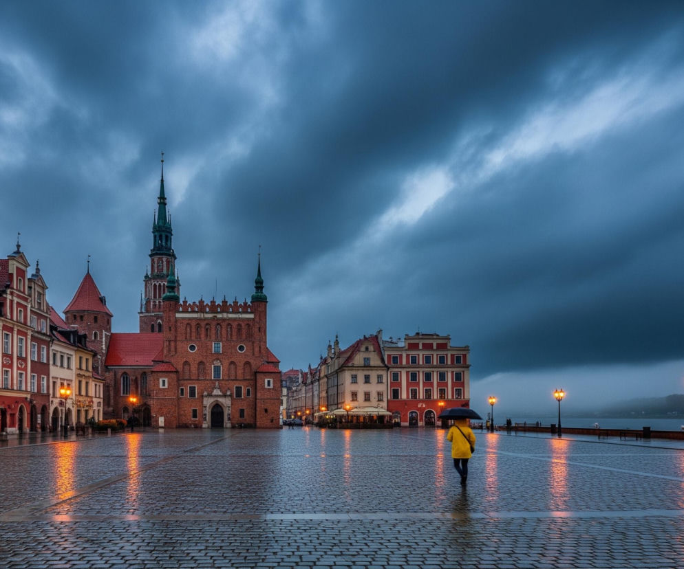 Centralną część obrazu zajmuje duży, brukowany plac miejski, pokryty deszczem, co widać po odbiciach świateł latarni i budynków w mokrej nawierzchni. Po prawej stronie placu idzie samotna osoba w jaskrawożółtym płaszczu, trzymająca czarny parasol. Tło stanowi rząd kamienic, z których wyróżnia się duży, ceglany budynek z wysoką, spiczastą wieżą pokrytą zielonym dachem pośrodku, a także kamienice w odcieniach czerwieni i beżu. Ciemne, ołowiane chmury dominują niebo, kontrastując z ciepłym blaskiem ulicznych latarni, które rzucają długie, pomarańczowe odbicia na mokrym bruku.