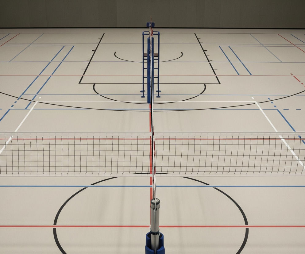 W centrum zdjęcia znajduje się siatka do siatkówki, rozciągnięta między dwoma słupkami o srebrnej i niebieskiej barwie, dzieląca beżową podłogę hali sportowej. Podłoga jest pokryta licznymi, wyraźnymi liniami w kolorach czarnym, czerwonym, białym i niebieskim, wyznaczającymi różne boiska, w tym charakterystyczne łuki i prostokąty boiska do koszykówki za siatką. W tle widać ciemnoszarą ścianę, która ciągnie się wzdłuż górnej części obrazu.