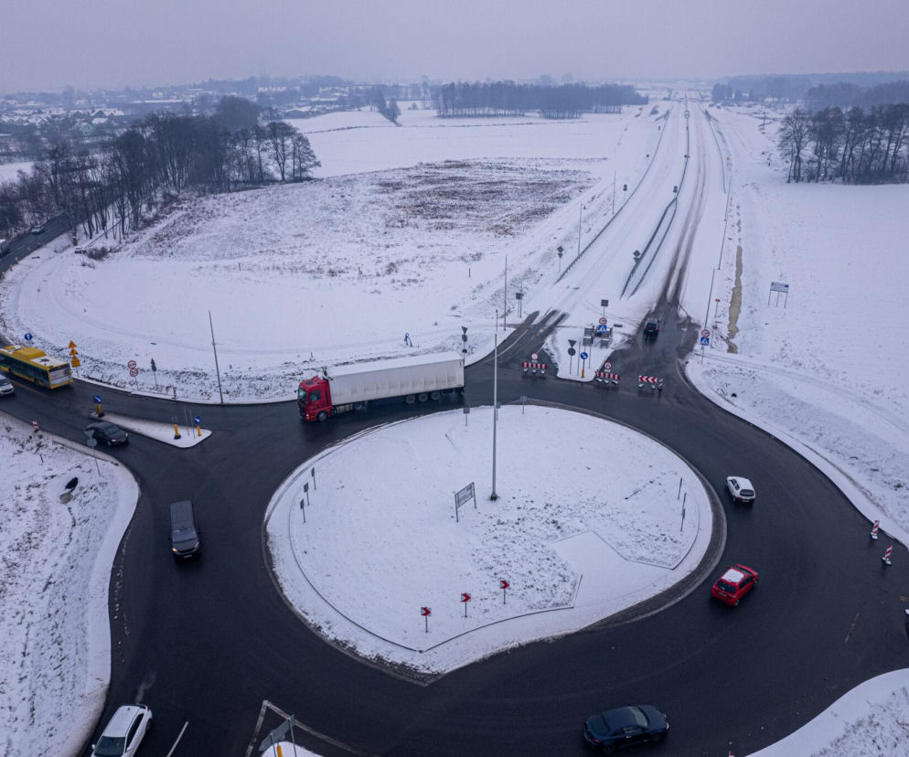 Zimowy widok z drona na budowę S1 Bieruń – Oświęcim, gdzie powstaje nowy węzeł drogowy. Na zdjęciu ośnieżone pola, fragment obwodnicy, rondo z poruszającymi się autami oraz żółtym autobusem. Więcej o infrastrukturze drogowej na Architektura Murator Plus.