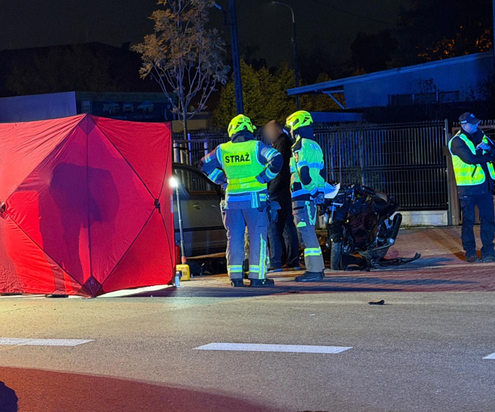 Strażacy i policjanci przy czerwonym parawanie i rozbitym motorze. O wypadku w Łomiankach przeczytasz na SE.