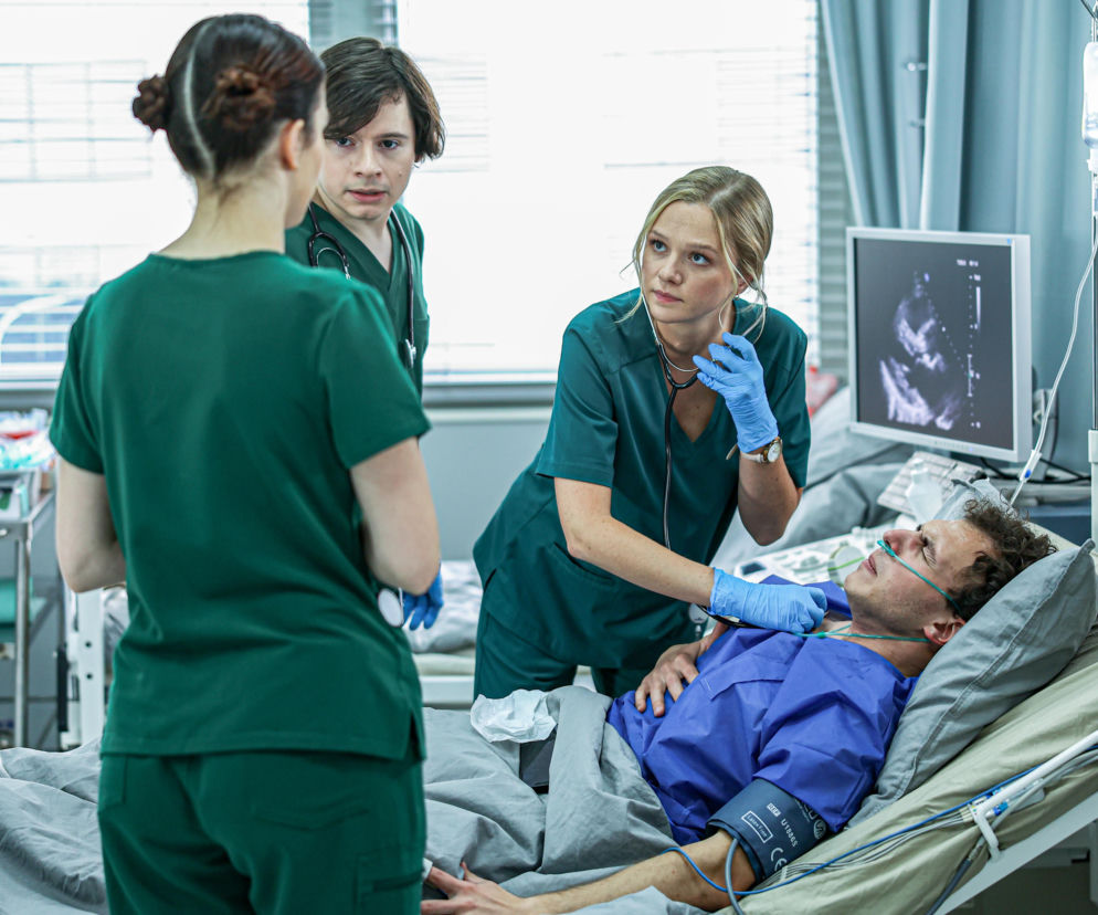 Lekarka Kaja Piotrowska bada stetoskopem leżącego pacjenta. O serialu Szpital św. Anny przeczytasz na Eska.