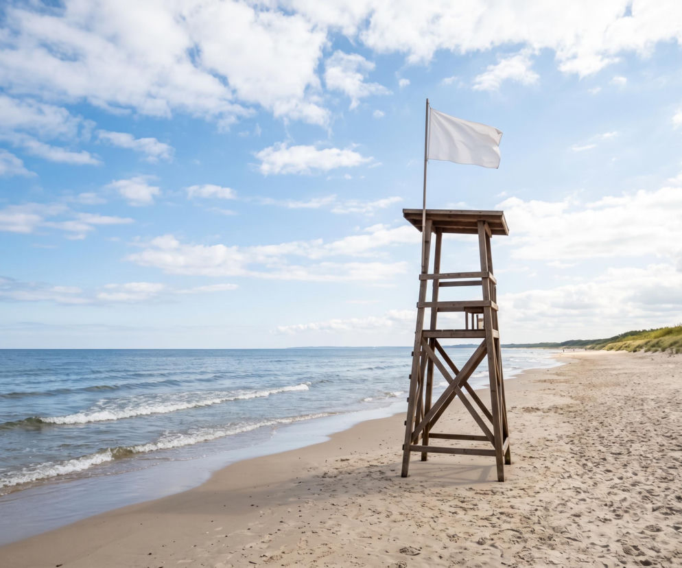 Drewniana wieża ratownicza z białą flagą na piaszczystej plaży w Świnoujściu. O czystej wodzie przeczytasz na SE Szczecin.