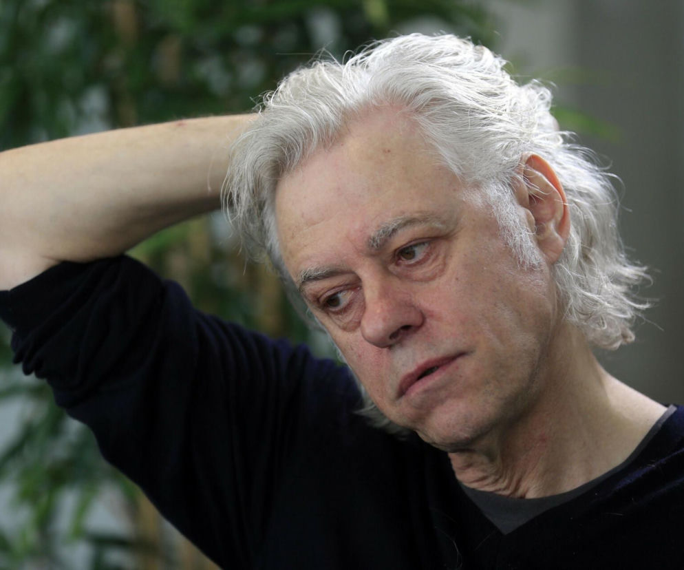 Zamyślony Bob Geldof trzyma rękę za głową i patrzy w dół. O historii muzyka i aktywisty przeczytasz na EskaRock.