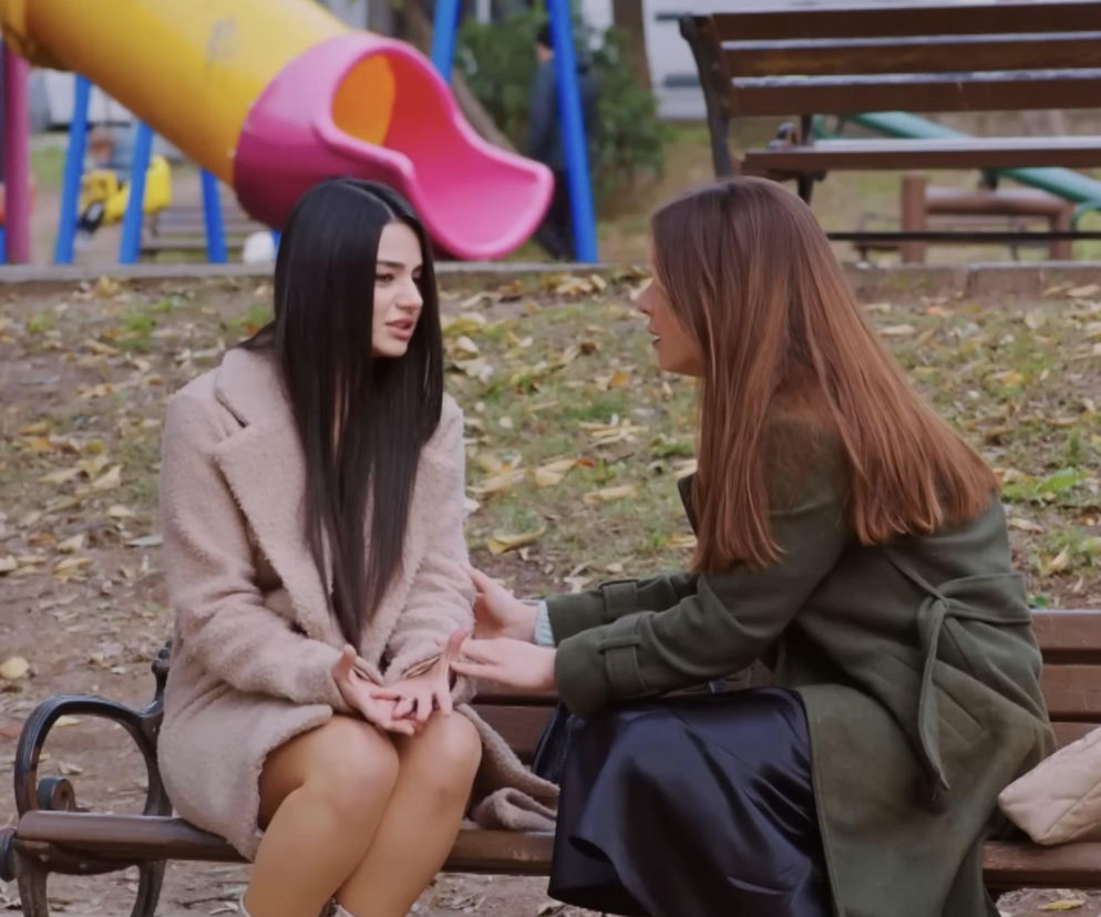 Dwie kobiety, Bahar i Sila z serialu Miłość i nadzieja, siedzą na ławce w parku. Kobieta z prawej (Bahar) w zielonym płaszczu i granatowej spódnicy, z brązowymi włosami, trzyma dłonie kobiety z lewej (Sila) w beżowym płaszczu, z długimi, czarnymi włosami. W tle widać plac zabaw i nagie drzewa. Scena szczerej rozmowy Sili i Bahar, opisana w Super Seriale.