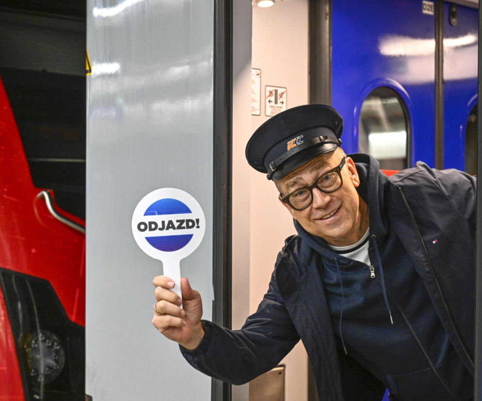 Uśmiechnięty Maciej Orłoś w czapce konduktora trzyma lizak z napisem ODJAZD. O emeryturze dziennikarza przeczytasz na SE.