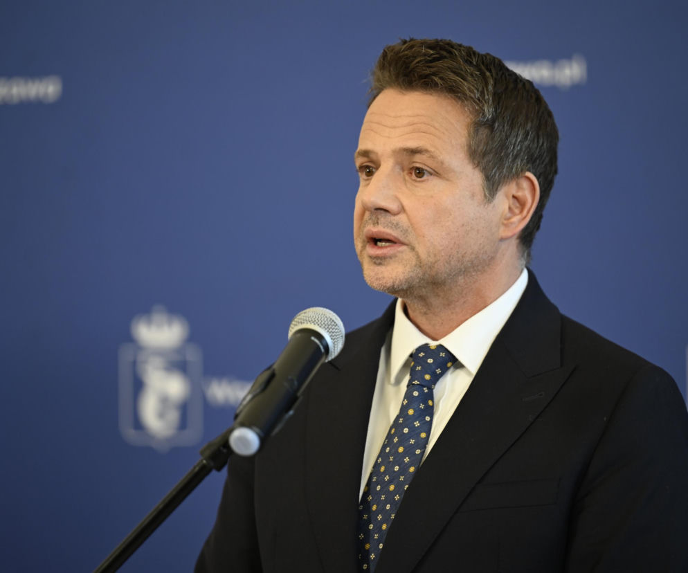 Prezydent Rafał Trzaskowski przemawiający podczas posiedzenia Rady Miejskiej, w tle widoczne logo Warszawy. Trzaskowski, ubrany w garnitur i krawat, zabiera głos w sprawie nieprawidłowości w Szpitalu Południowym, o czym możesz przeczytać na naszym portalu.
