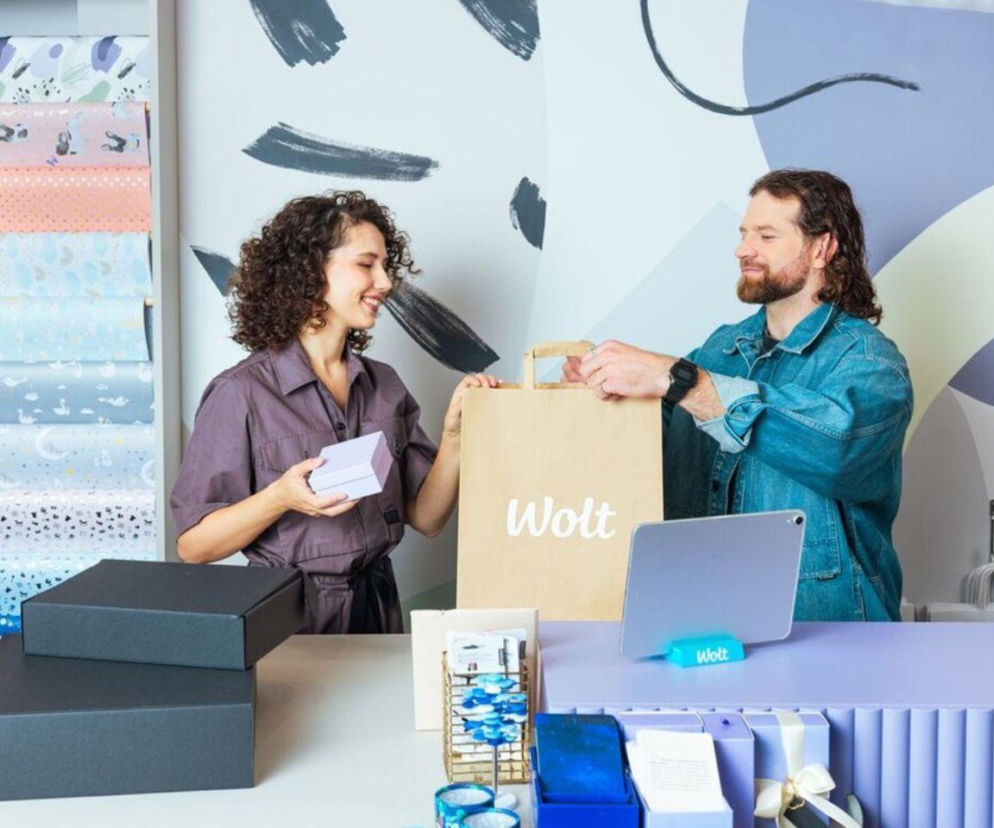 Uśmiechnięta kobieta i mężczyzna trzymają papierową torbę z logo Wolt. O nowym raporcie retail przeczytasz w Eska.