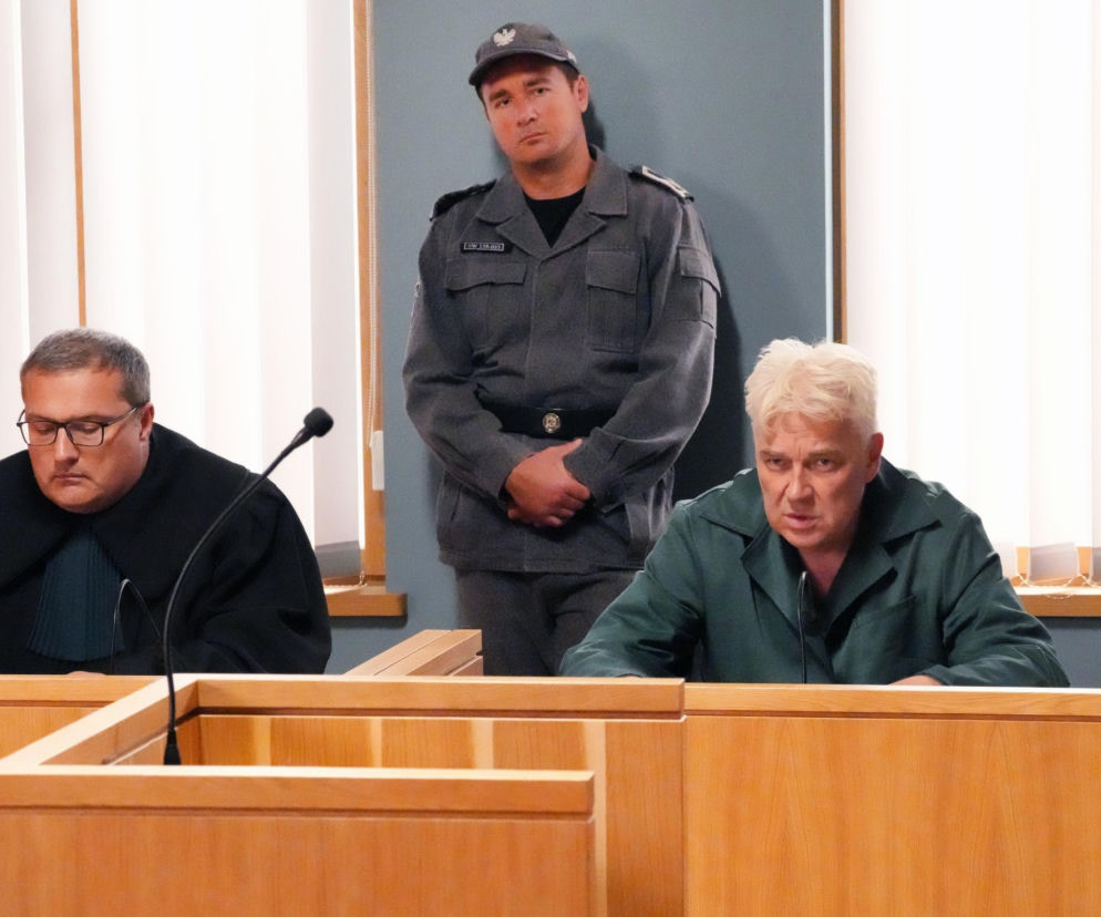 Sala sądowa, w tle stojący strażnik więzienny w szarym mundurze, z przodu dwaj mężczyźni przy drewnianych ławach. Jeden w czarnej todze, drugi z siwymi włosami, w zielonym ubraniu więziennym, wyglądający na zatroskanego. Dowiedz się więcej o Barwy Szczęścia na Super Seriale.