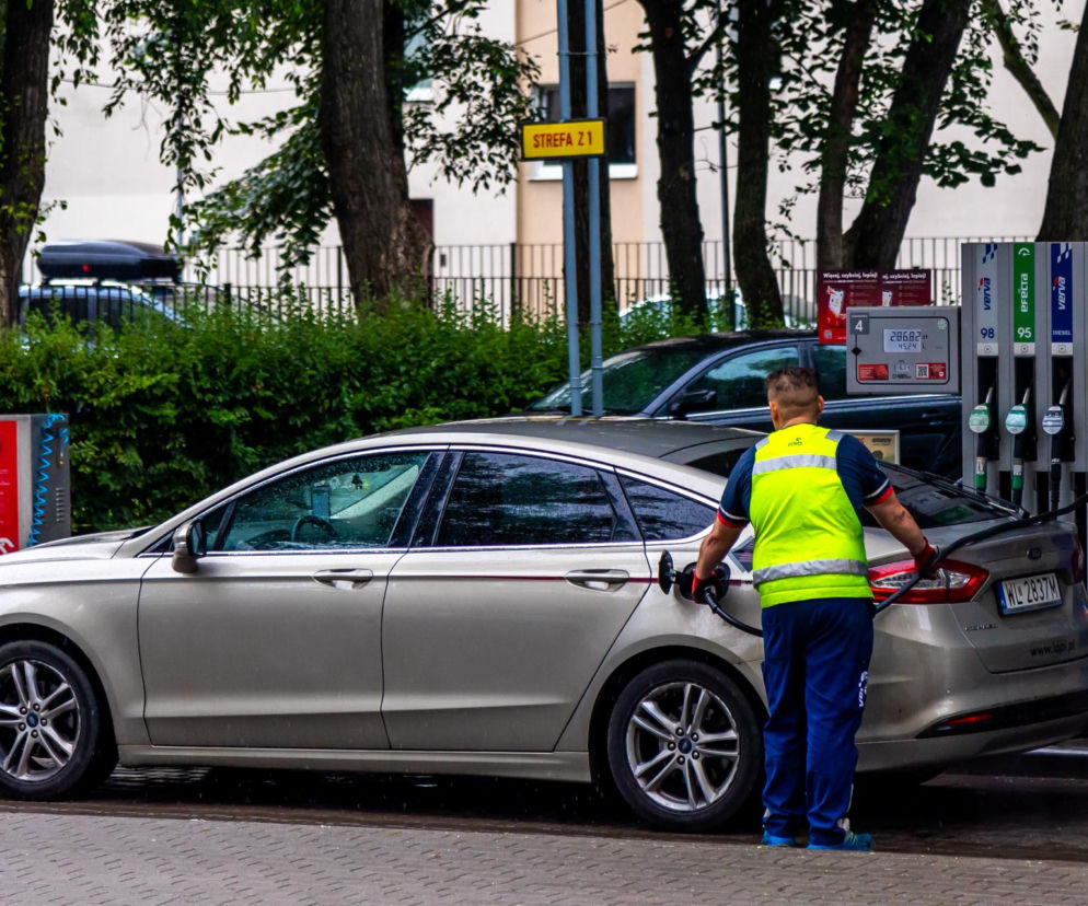 Pracownik stacji paliw tankuje srebrny samochód. O rosnących podatkach na benzynę przeczytasz na SE Superbiz.