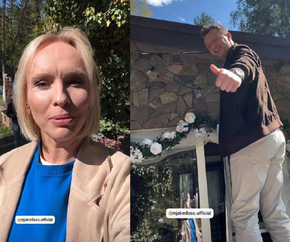 Iwona Rejzner w blond włosach i niebieskiej bluzie na planie serialu oraz Arkadiusz Smoleński, uśmiechnięty w brązowej kurtce i jasnych spodniach, pokazujący kciuk w górę. Aktorzy przygotowują ślubne dekoracje w siedlisku, co oznacza zbliżającą się ceremonię, o której przeczytasz więcej na Super Seriale.