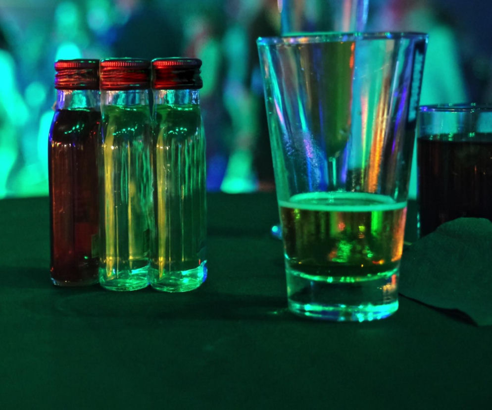 Trzy małe butelki alkoholu i szklanki na stole w klubie. O planowanym zakazie sprzedaży małpek przeczytasz na Eska.
