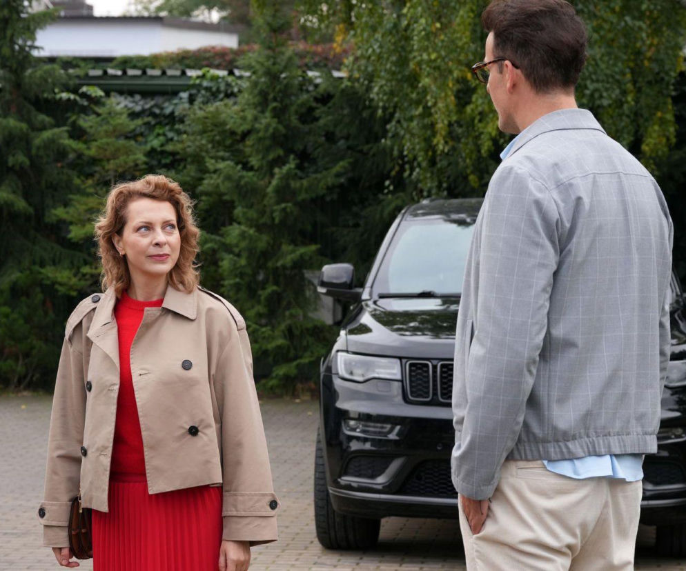 Dorota (Karina Seweryn) w beżowym płaszczu i czerwonej sukience patrzy na odwróconego plecami Radomira (Łukasz Wójcik) w szarej kurtce. Spotkanie dwojga bohaterów serialu Barwy szczęścia na zewnątrz domu. Więcej o ich relacji dowiesz się na Super Seriale.