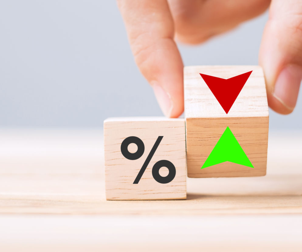 Ręka układająca drewniane klocki z symbolem procentu oraz strzałkami w górę i w dół, co symbolizuje zmiany w oprocentowaniu kredytów i zamiennik WIBOR. O reformie wskaźników referencyjnych przeczytasz na Super Biznes.