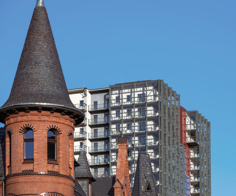 Zabytkowa ceglana wieża Browarów Wrocławskich na tle nowoczesnych apartamentowców. O inwestycji przeczytasz na Architektura.
