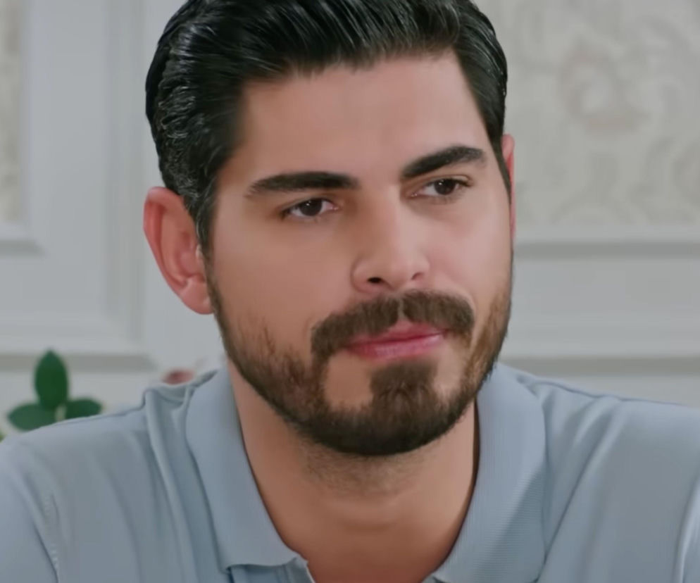 Młody mężczyzna, Türkseve, w szarej koszulce polo, z ciemnymi włosami i brodą, patrzy w prawo z delikatnym uśmiechem. Zdjęcie przedstawia Cihana, jednego z głównych bohaterów serialu „Panna młoda”, o którym można przeczytać na Super Seriale.