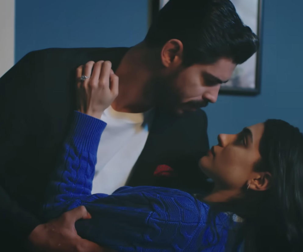 Cihan trzymający Hancer w ramionach, ich twarze są blisko, spojrzenia intensywne, oboje mają ciemne włosy, Hancer ma na sobie niebieski sweter, a Cihan ciemną marynarkę, białą koszulkę i poszetkę. Scena z serialu Panna młoda zwiastuje przełom w ich relacji, o czym przeczytasz na Super Seriale.