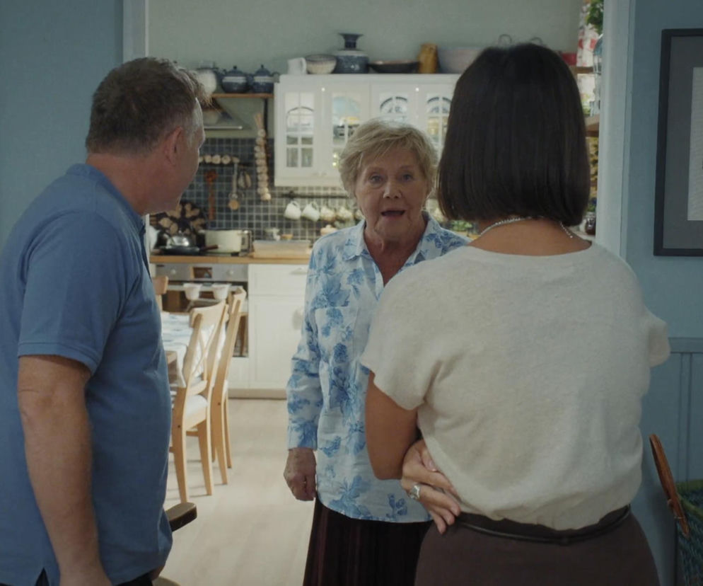 Barbara Mostowiak (Teresa Lipowska) w kwiecistej koszuli, z zaskoczeniem patrzy na Artura Rogowskiego (Robert Moskwa) i Agnes (Amanda Mincewicz), stojących tyłem. Scena z odcinka M jak miłość, gdzie Barbara przewiduje działania Agnes, co możesz przeczytać na Super Seriale.