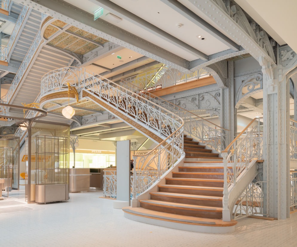 Wnętrze luksusowego domu handlowego La Samaritaine w Paryżu z odrestaurowanymi, krętymi schodami i kutymi balustradami w stylu art déco, jasnym światłem i eleganckimi detalami. Więcej o architekturze wnętrz na Architektura Murator Plus.