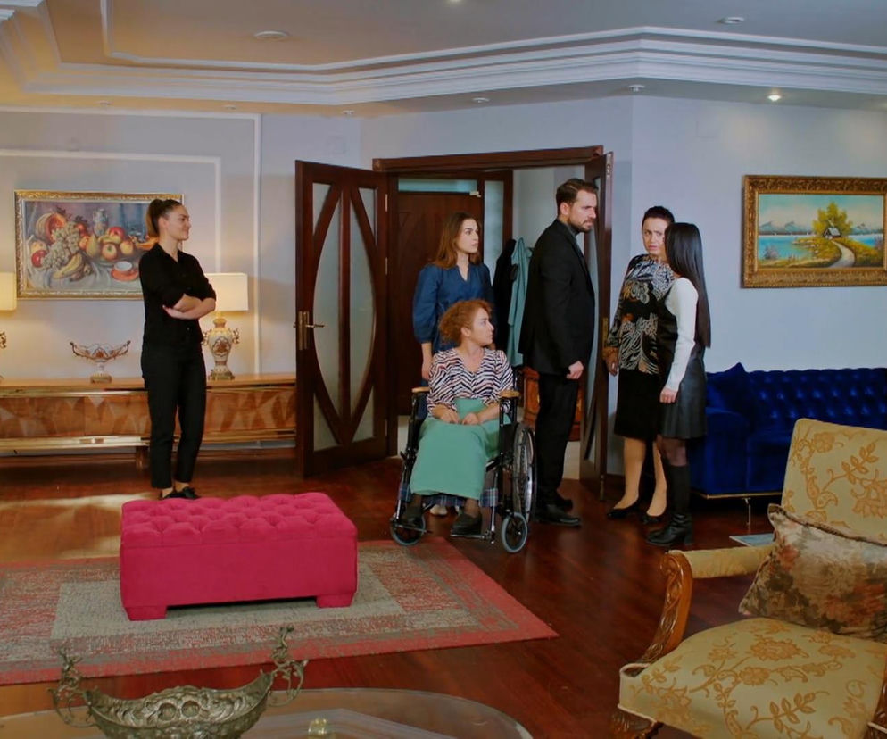 Sila ze skrzyżowanymi rękami stoi po lewej stronie eleganckiego salonu, patrząc na pozostałe postacie. Hulya na wózku inwalidzkim patrzy w prawo, otoczona Kuzeyem, Bahar i Cavidan, które stoją obok otwartych drzwi. Hulya właśnie ujawniła prawdę o wypadku, co wywołało konfrontację w rezydencji Bozbeyów, a wszystkie szczegóły znajdziesz na Super Seriale.