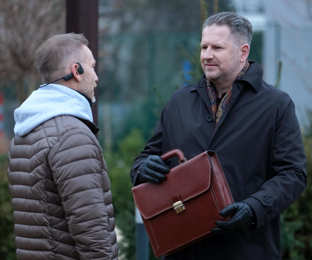 Igor Jabłoński (Marcin Piętowski) oferuje Andrzejowi Budzyńskiemu (Krystian Wieczorek) teczkę z pieniędzmi w serialu M jak miłość. Zdjęcie to ilustruje dramatyczną scenę z odcinka 1925, gdzie prawnik mierzy się z pokusą przekupstwa. Więcej o losach bohaterów na Super Seriale.