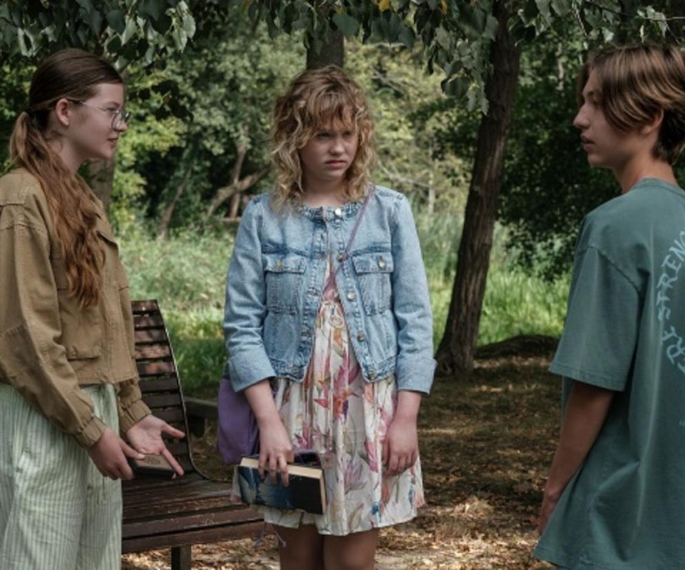 Trójka nastolatków w parku. Emilka (Jessica Frankiewicz) w okularach i beżowej kurtce rozmawia z Polą (Gabriela Szewczyk), ubraną w kwiecistą sukienkę i jeansową kurtkę. Obok stoi Emil (Artem Malaszczuk) w zielonej koszulce. Zdjęcie ilustruje emocje związane z serialem Barwy Szczęścia, o którym przeczytasz więcej na Super Seriale.