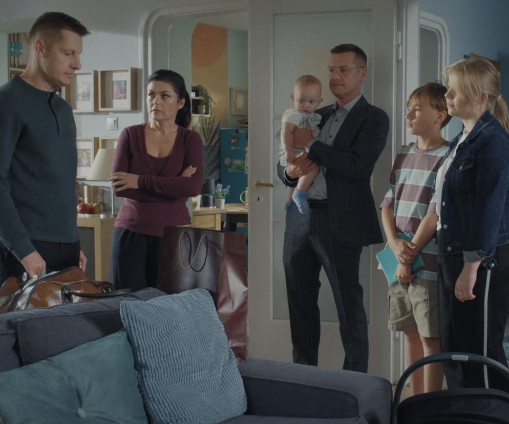 Paweł Zduński stoi w salonie z torbą podróżną, obok niego Kinga z założonymi rękami. W drzwiach stoi Piotrek Mroczek trzymający na rękach niemowlę, a obok niego dzieci: Lenka i Misiek. Cała scena dotyczy emocjonalnego momentu w serialu, opisanego na Super Seriale.