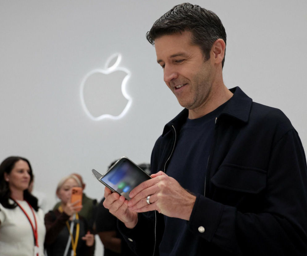 Mężczyzna trzyma składany telefon na tle logo Apple. O nowościach iPhone 18 Pro przeczytasz na Eska.