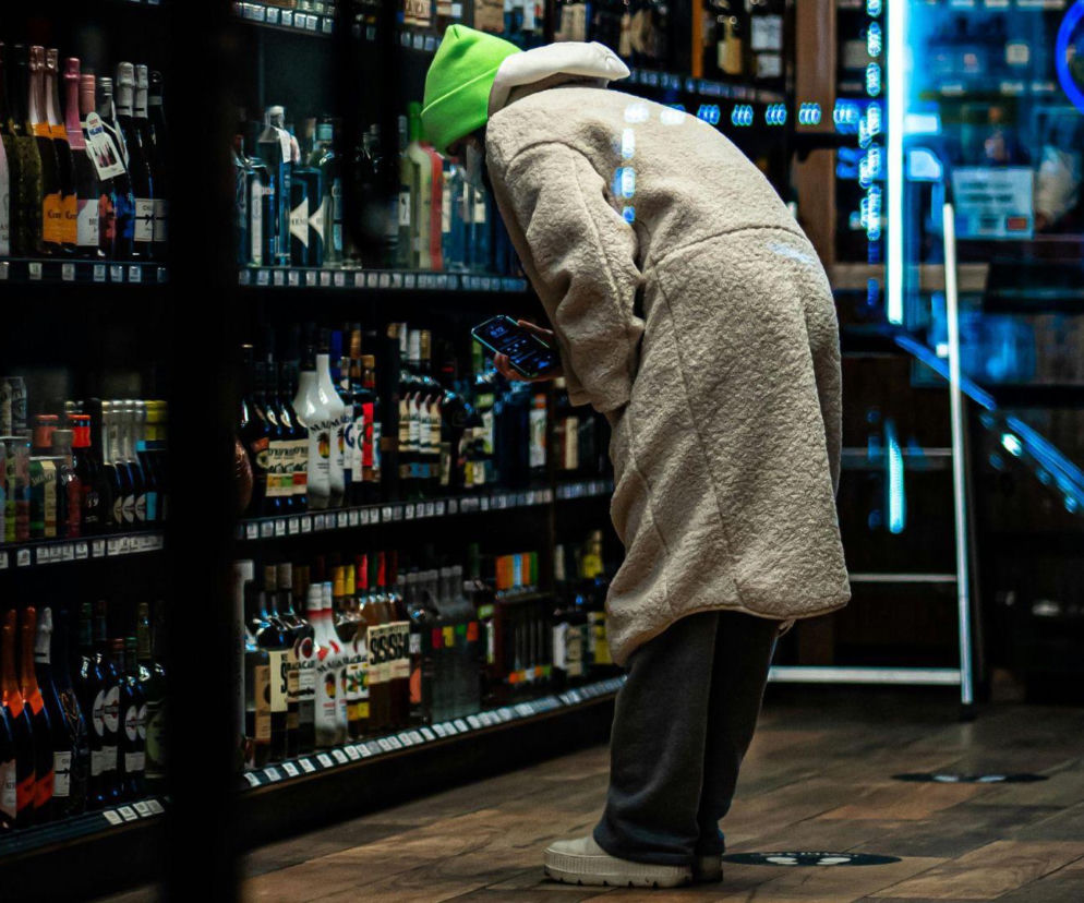 Osoba w beżowym płaszczu wybiera alkohol w sklepie nocą. O konsultacjach w Gliwicach przeczytasz na Eska.