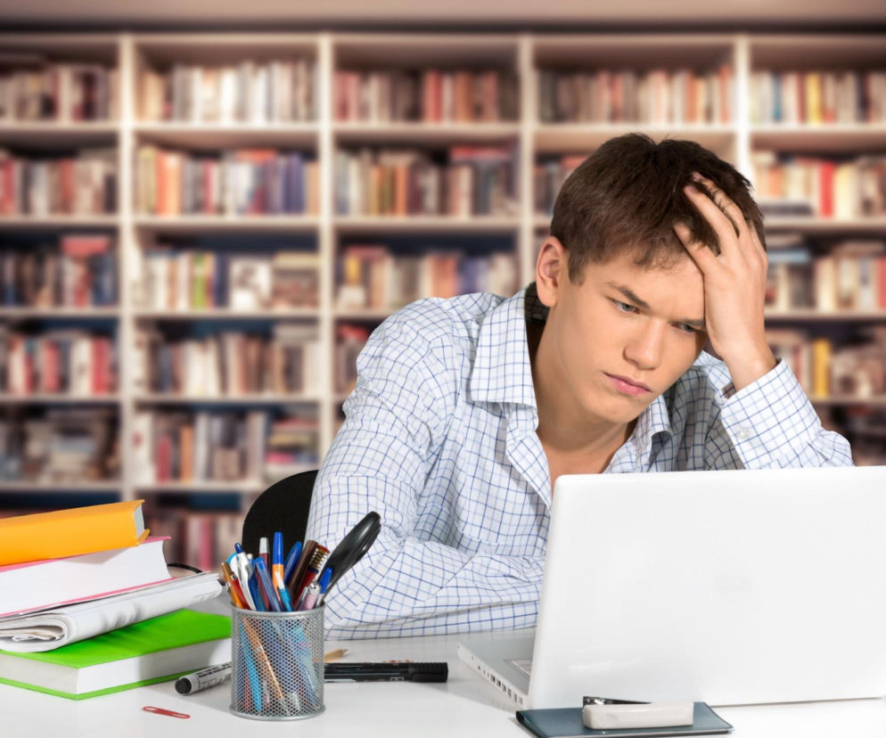 Zamyślony student przy laptopie w bibliotece. O planowaniu budżetu na studia przeczytasz na Eska.