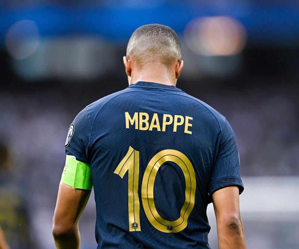 Kylian Mbappé, francuski piłkarz z numerem 10 na koszulce, odwrócony plecami, symbolizujący walkę o sukces w fazie pucharowej Mistrzostw Świata. Na naszym portalu znajdziesz szczegółowe analizy meczów i wyniki.